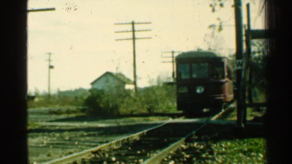 1953 Connecticut 8mm frame showing the trolley nearing the foreground track area, with rural brush, utility poles, and a small house behind.