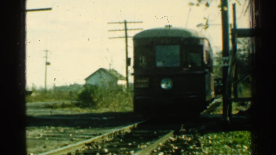 1953 Connecticut 8mm frame with the red trolley close to the camera on rural tracks, its front light area visible against a faded background.
