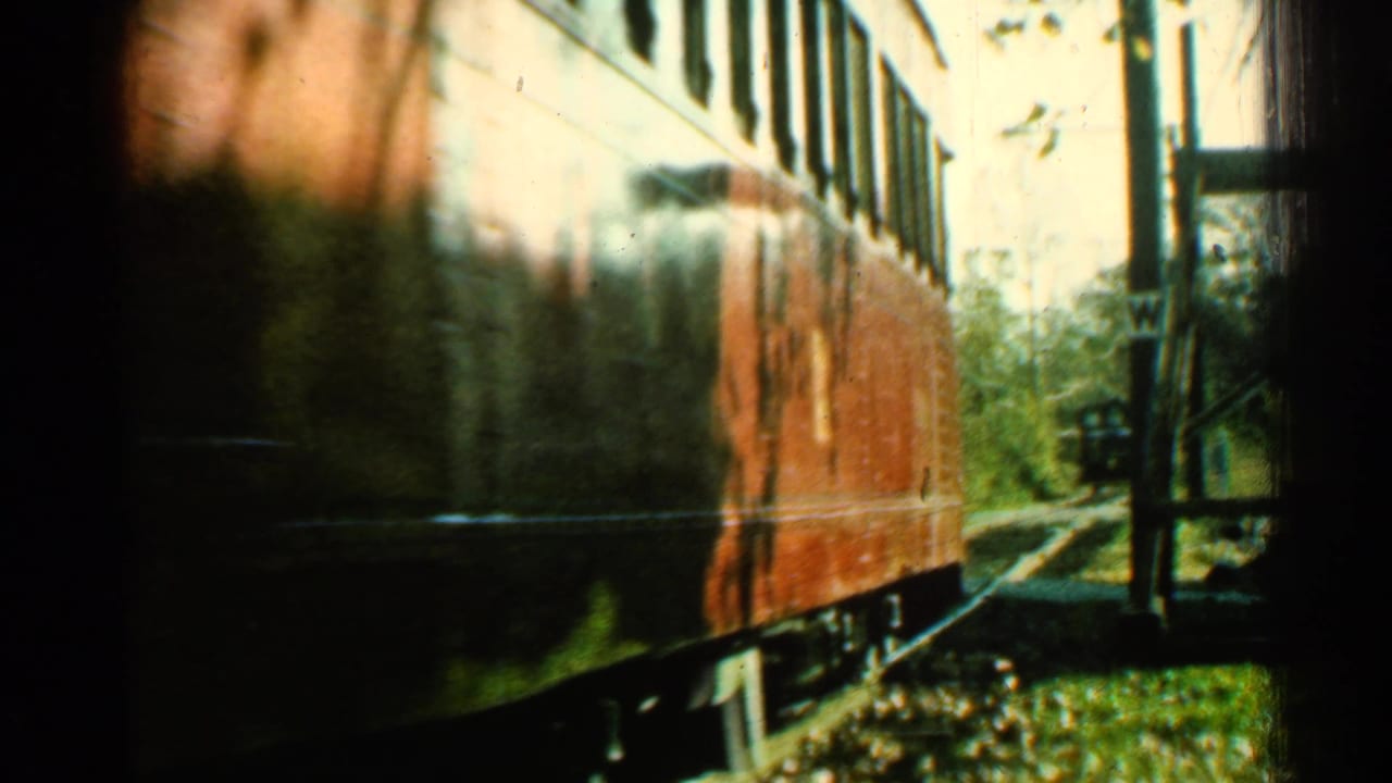 The red rail car passes close to the fixed camera, with its side filling the frame and trackside structures visible at the edge.