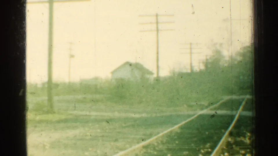 A faded 8mm frame shows the track curving away past brush, utility poles, and a small house in bright Connecticut daylight.