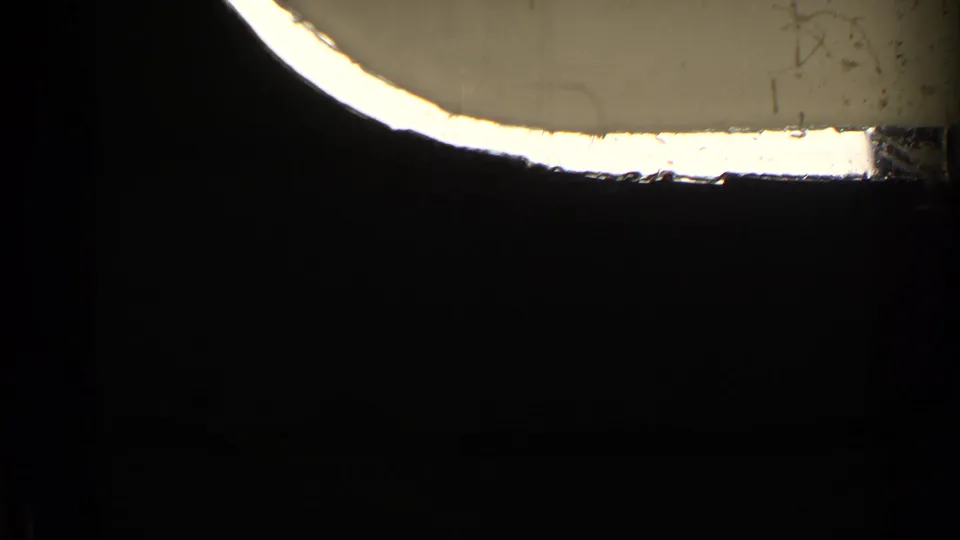 A mostly dark 8mm frame where the train-window or film-gate edge creates a bright curved band across the upper portion.