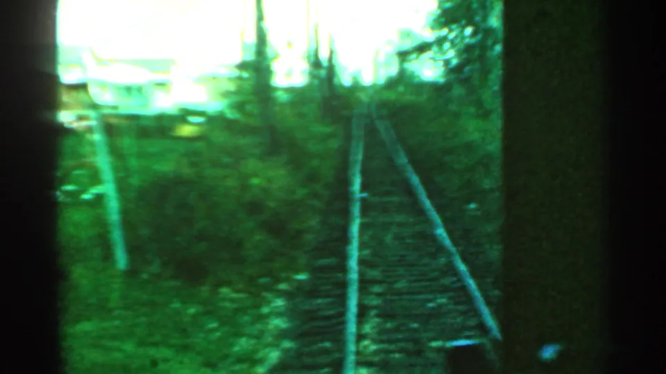 Green-tinted 1953 Connecticut rail view with tracks curving through trees, utility poles, and an overexposed building shape ahead.