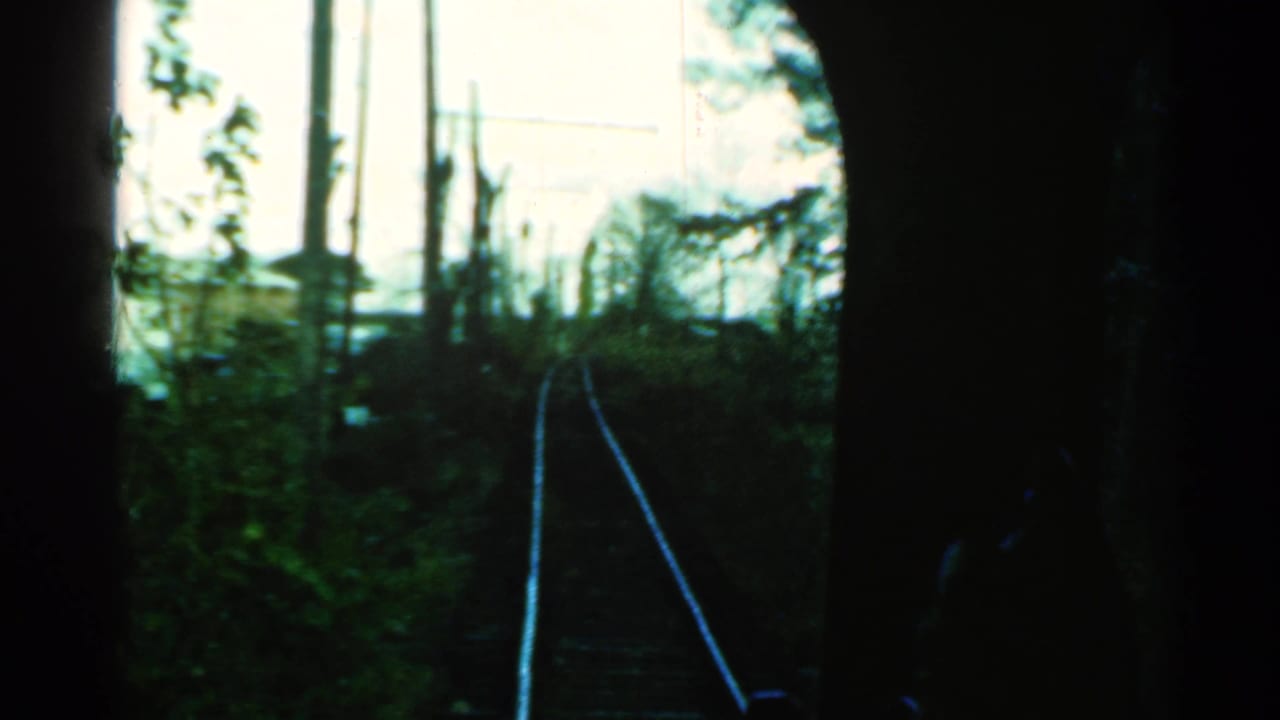 1953 Connecticut home-movie view from a moving train window, looking along tracks through dark framing toward trees and utility poles.