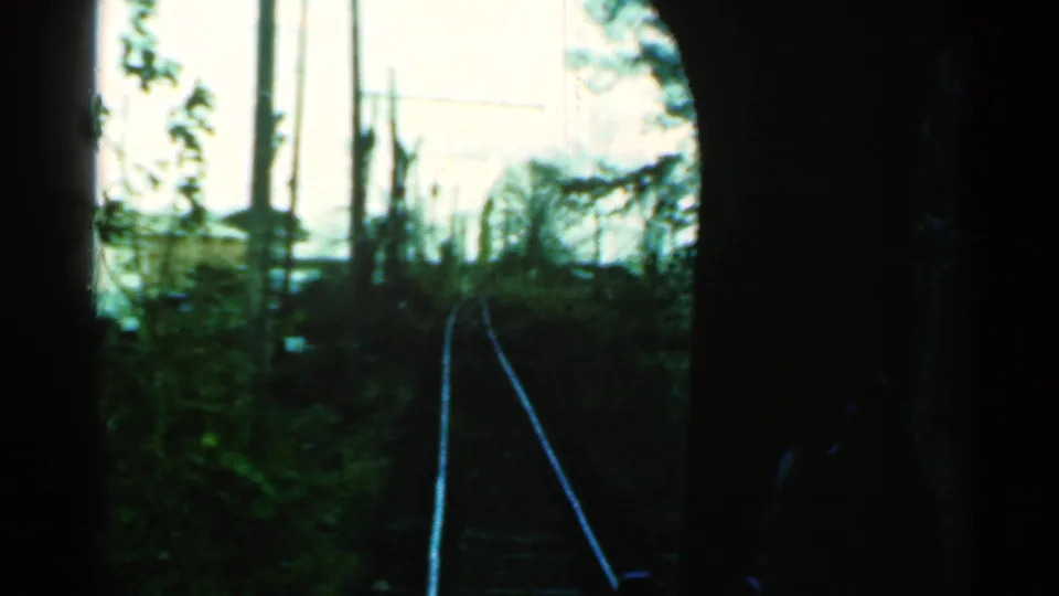 1953 Connecticut home-movie view from a moving train window, looking along tracks through dark framing toward trees and utility poles.