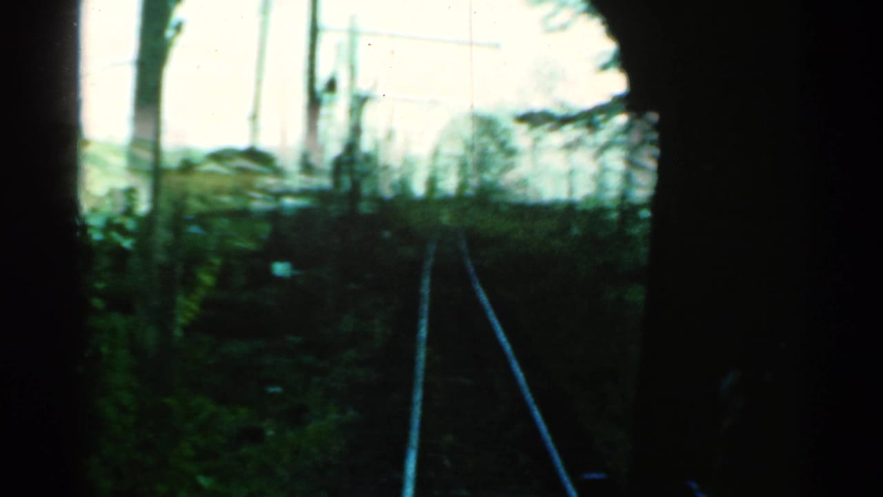 Moving train view in Connecticut, with tracks curving through brush and poles under a bright sky, framed by dark interior edges.