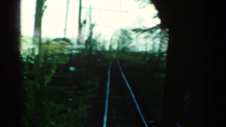 Moving train view in Connecticut, with tracks curving through brush and poles under a bright sky, framed by dark interior edges.