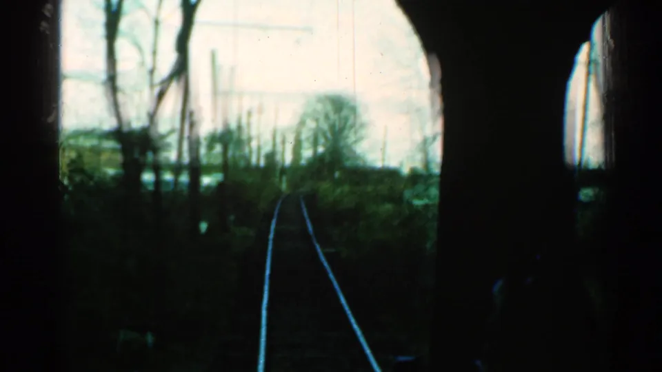 Forward-facing 8mm train view in Connecticut, with rails, bare trees, and utility poles visible beyond the dark window edge.