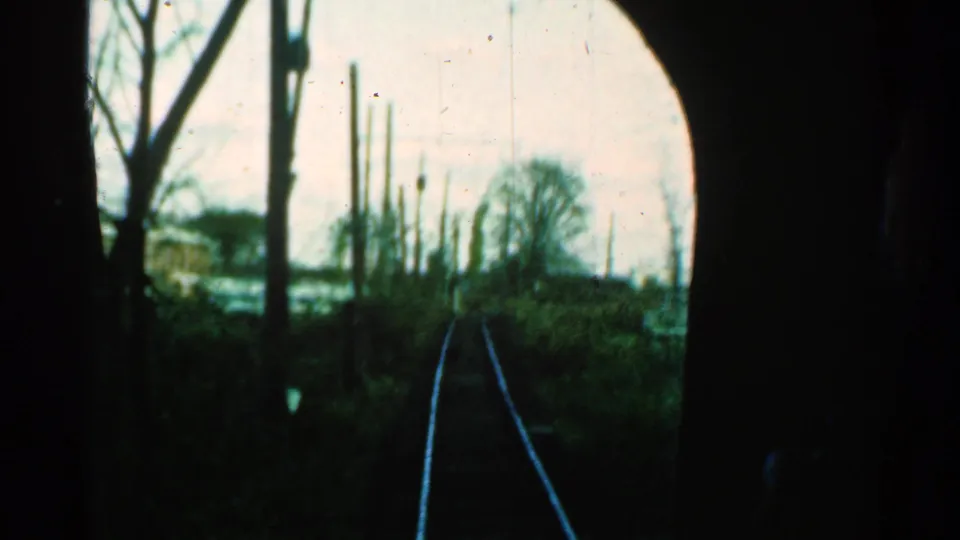 Archival 8mm frame from a 1953 Connecticut train journey, showing tracks ahead through bare trees and trackside brush.