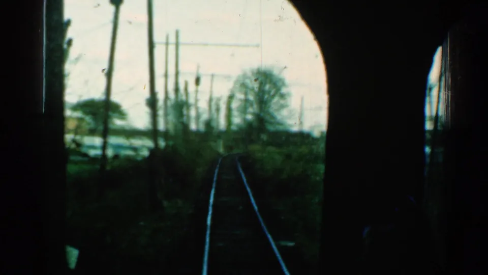1953 Connecticut home-movie frame looking ahead from a train at rails passing through a wooded trackside area.