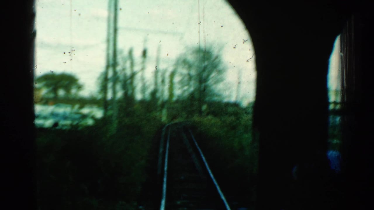 Home-movie train-window view in Connecticut, with dark framing around curving rails, utility poles, winter trees, and trackside vegetation.