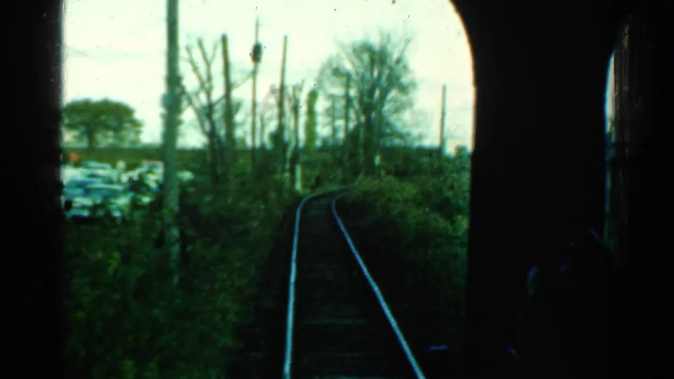 1953 Connecticut rail footage from a passenger viewpoint, showing the track bending beside overgrown vegetation and a cluttered trackside area.