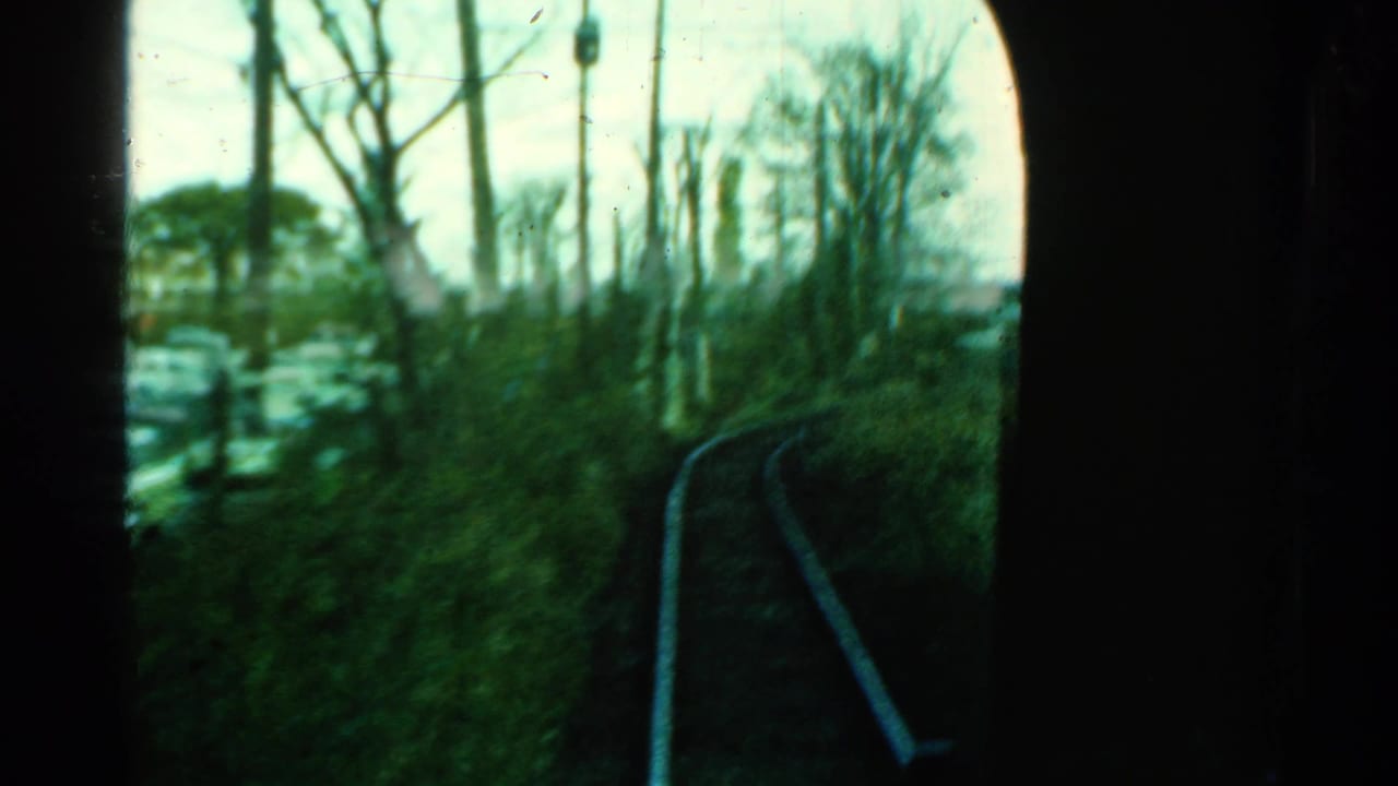 1953 Connecticut train-cab view through a dark arched window, showing curved rails, bare trees, utility poles, and trackside vegetation.