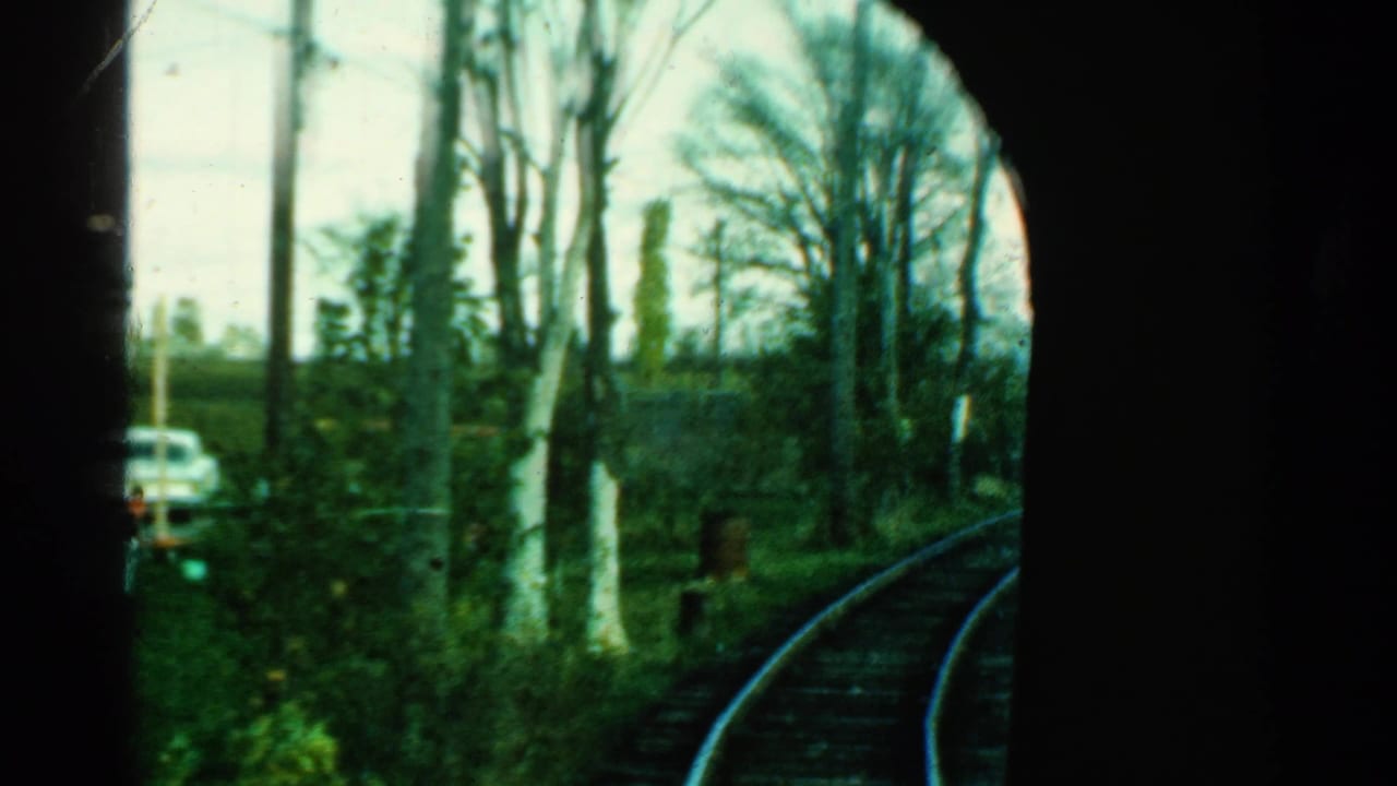 1953 Connecticut 8mm frame showing a passenger view past dark window framing toward curved rail track, leafless trees, grass, and a car.