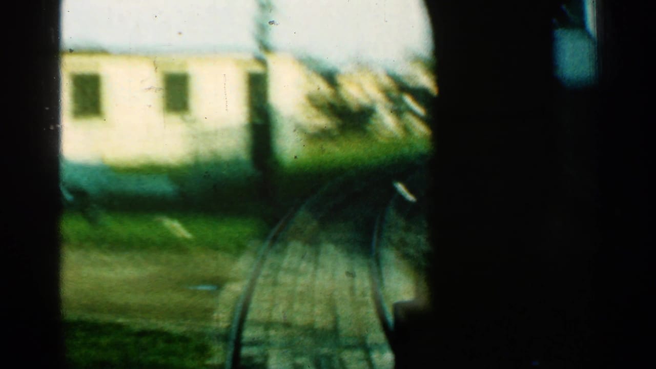 From inside the moving train, a soft 1953 Connecticut view shows curved track, pale rail-side building, grass, and heavy dark framing.