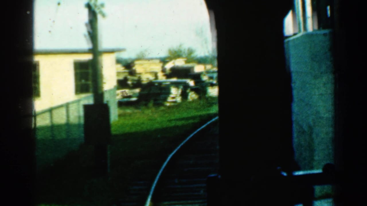 1953 Connecticut train-window view with dark interior framing, curved rail, grassy trackside area, utility poles, and stacked lumber or materials.