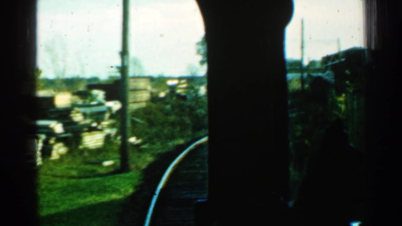 1953 Connecticut train-window view of curved rails, trackside grass, utility poles, and low buildings beyond the line.