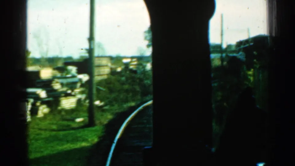 1953 Connecticut train-window view of curved rails, trackside grass, utility poles, and low buildings beyond the line.