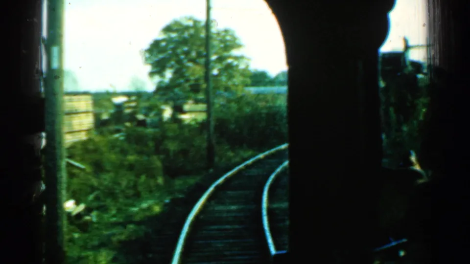1953 Connecticut rail journey view with curved track, grassy verge, fencing, a leafy tree, and dark carriage framing.