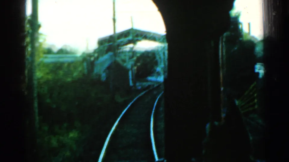 Passenger-view 8mm frame from Connecticut in 1953 showing rails, foliage, and a nearby concrete bridge-like structure.