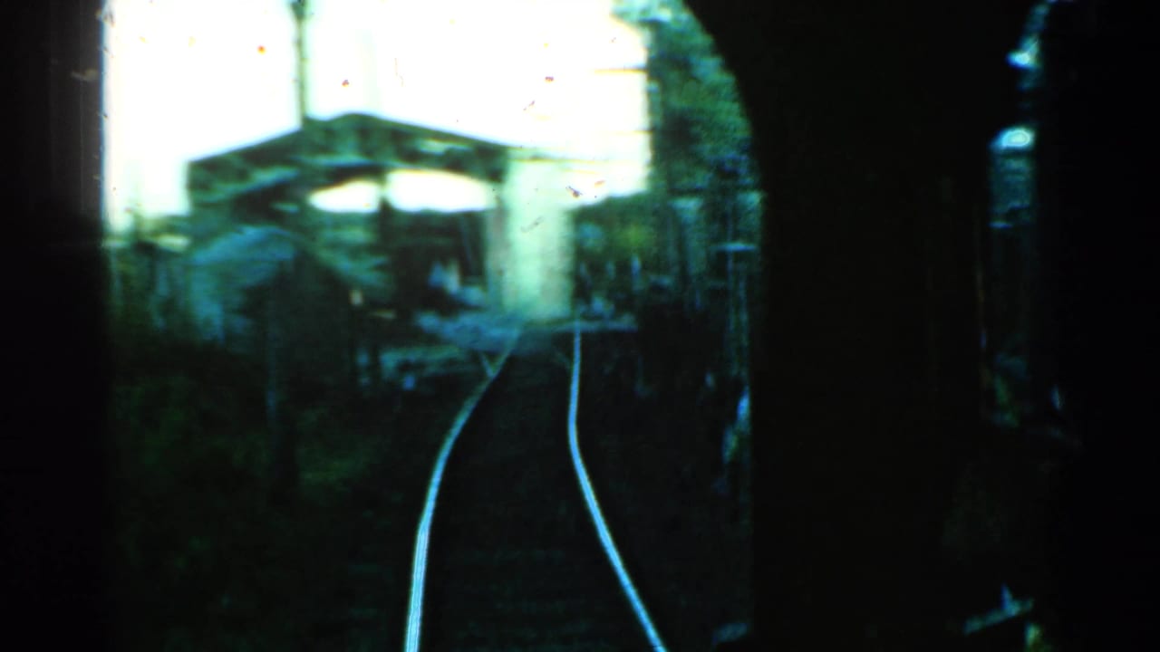Curving rail tracks viewed from a departing train near a small station structure.