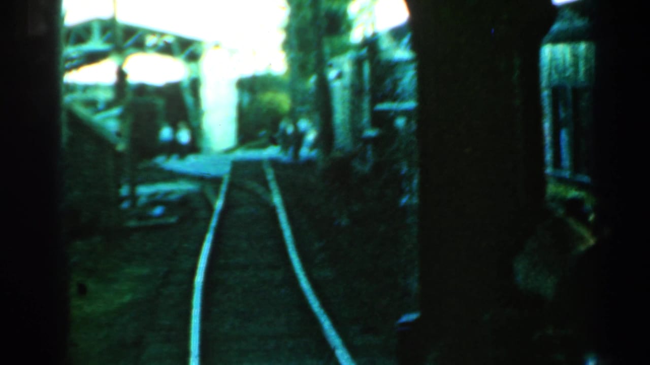 Rail tracks curve ahead beneath a metal overhead structure with dark train framing at the sides.