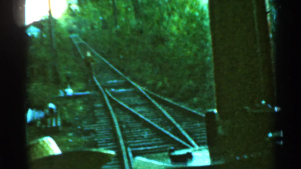 1953 Connecticut 8mm passenger view of tracks curving past wooded embankments with distant people near the line.
