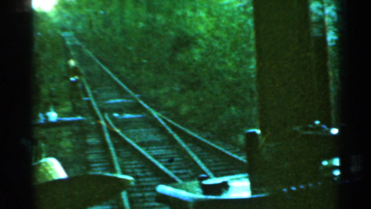 1953 Connecticut 8mm frame showing rails, switch equipment, and dense trees from an onboard train viewpoint.
