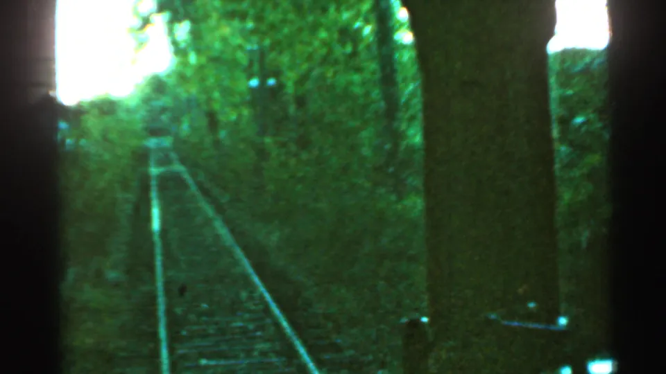Onboard 8mm view of Connecticut railroad tracks bordered by trees, with dark train-side structure framing the right side.
