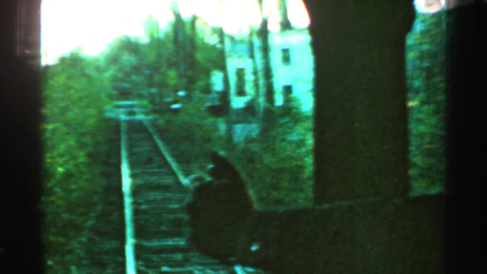 1953 Connecticut home-movie frame with tracks, trees, and a pale trackside building visible beyond the rail line.