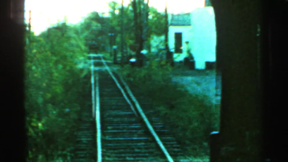 Connecticut 1953 8mm view of railroad tracks approaching a small white trackside building in a wooded setting.
