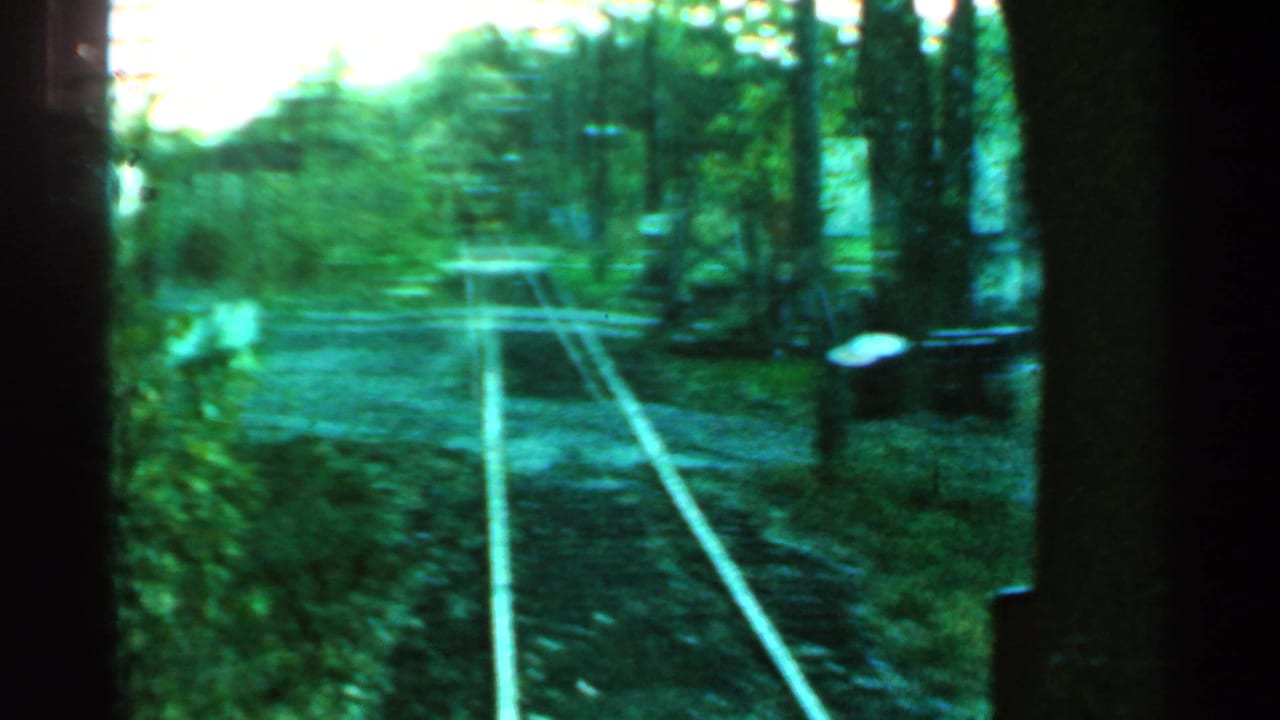 Rail tracks continue ahead past trees and a small light-colored building.