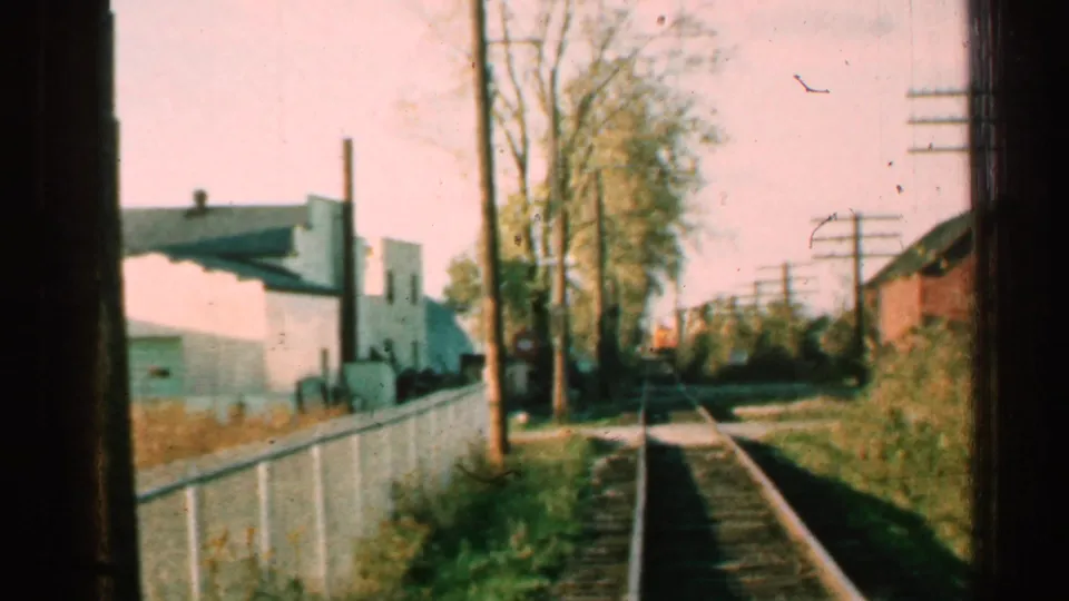 1953 Connecticut train point of view passing a fenced trackside stretch with utility poles, trees, and low buildings.