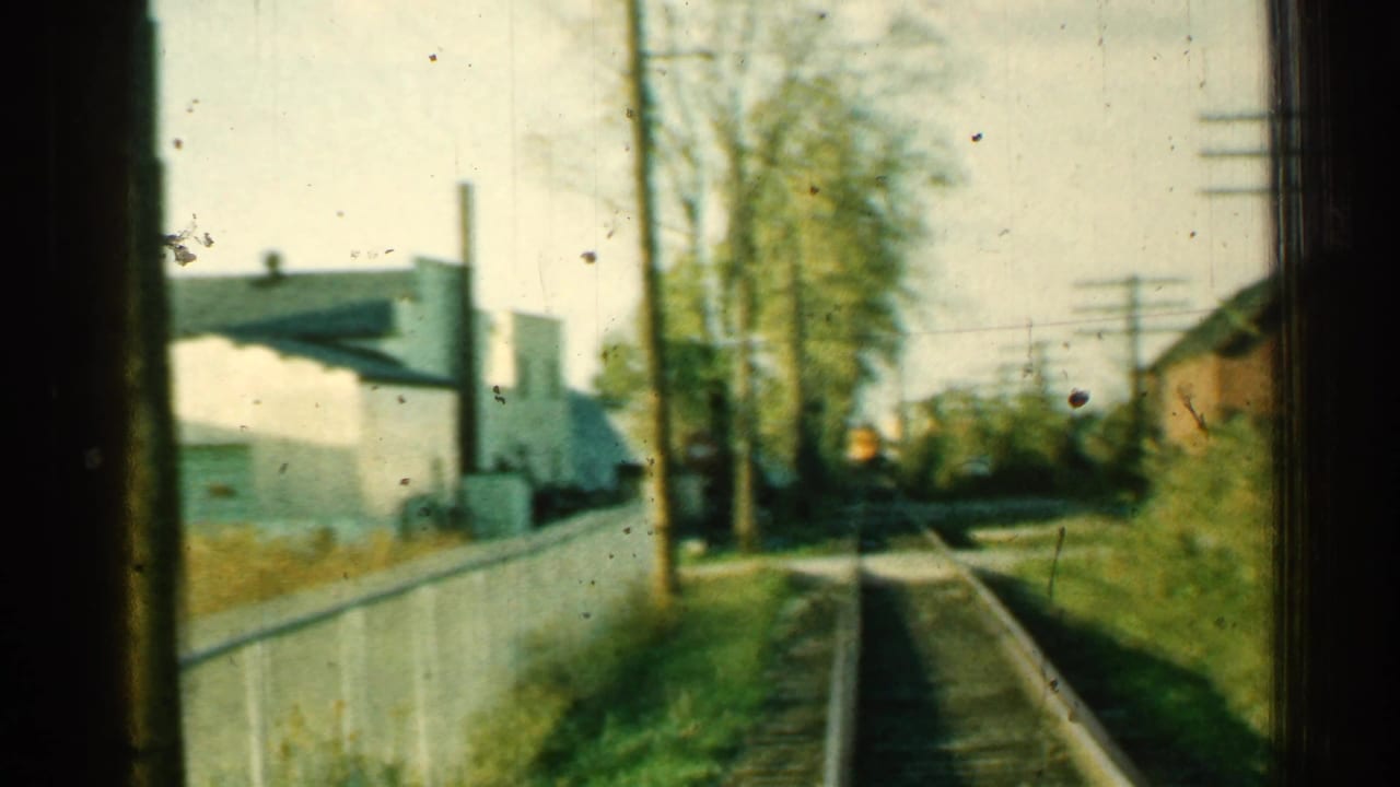 1953 Connecticut 8mm frame showing railroad tracks receding past a white fence, trees, utility poles, and low buildings.