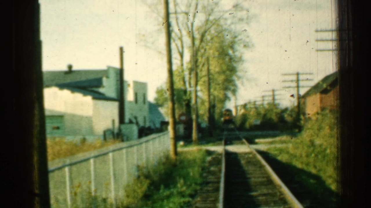 1953 Connecticut 8mm frame with a small distant train approaching along tracks through a suburban trackside view.