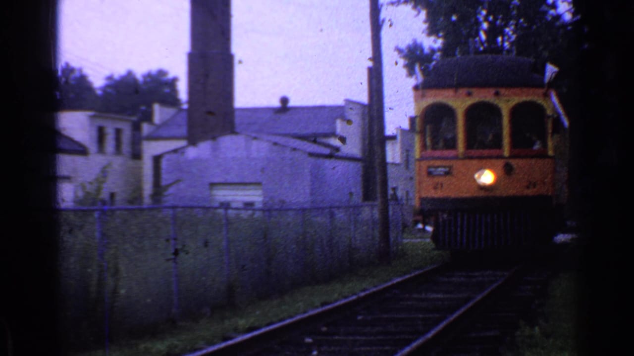 1953 Connecticut 8mm frame showing trolley car 21 approaching from a distance on rails near industrial buildings and fencing.