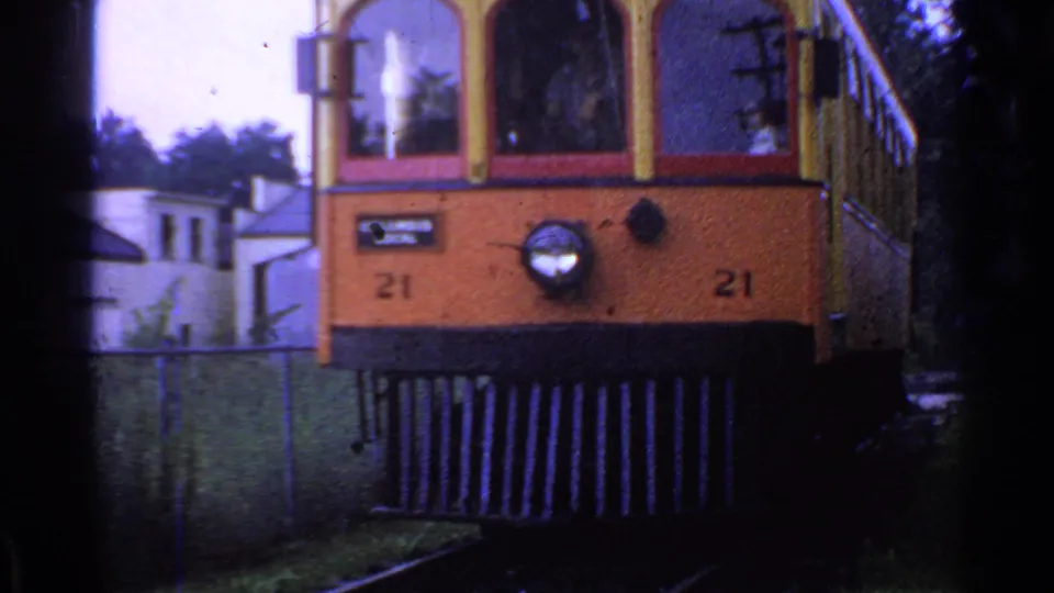 Close 8mm frame of trolley car 21 passing near the camera in Connecticut, with the headlight, front signage, rails, and fence visible.