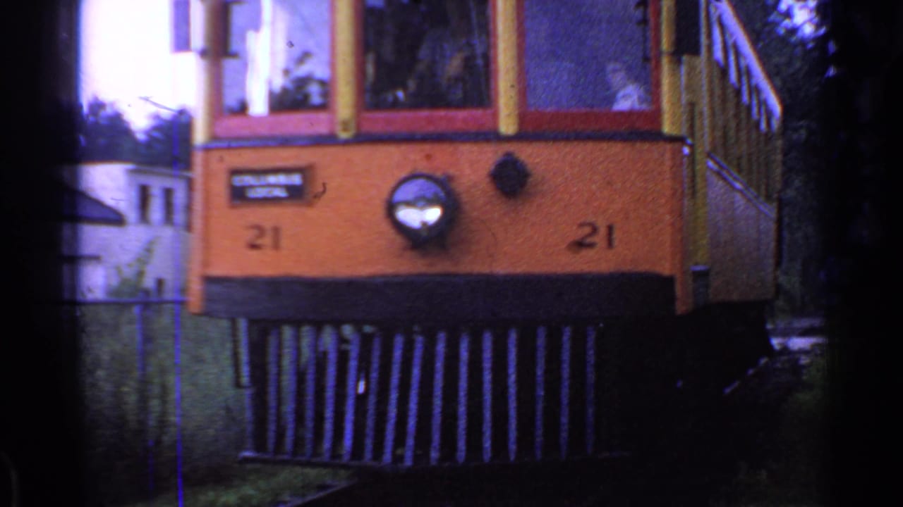 Orange and yellow trolley front marked 21 approaching through trees.
