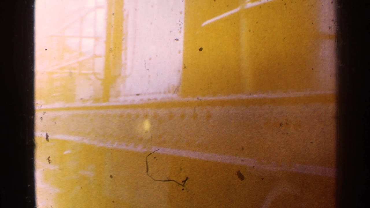 Warm light-leaked 8mm frame with a partial yellow railcar or structure and heavy film edge marks.