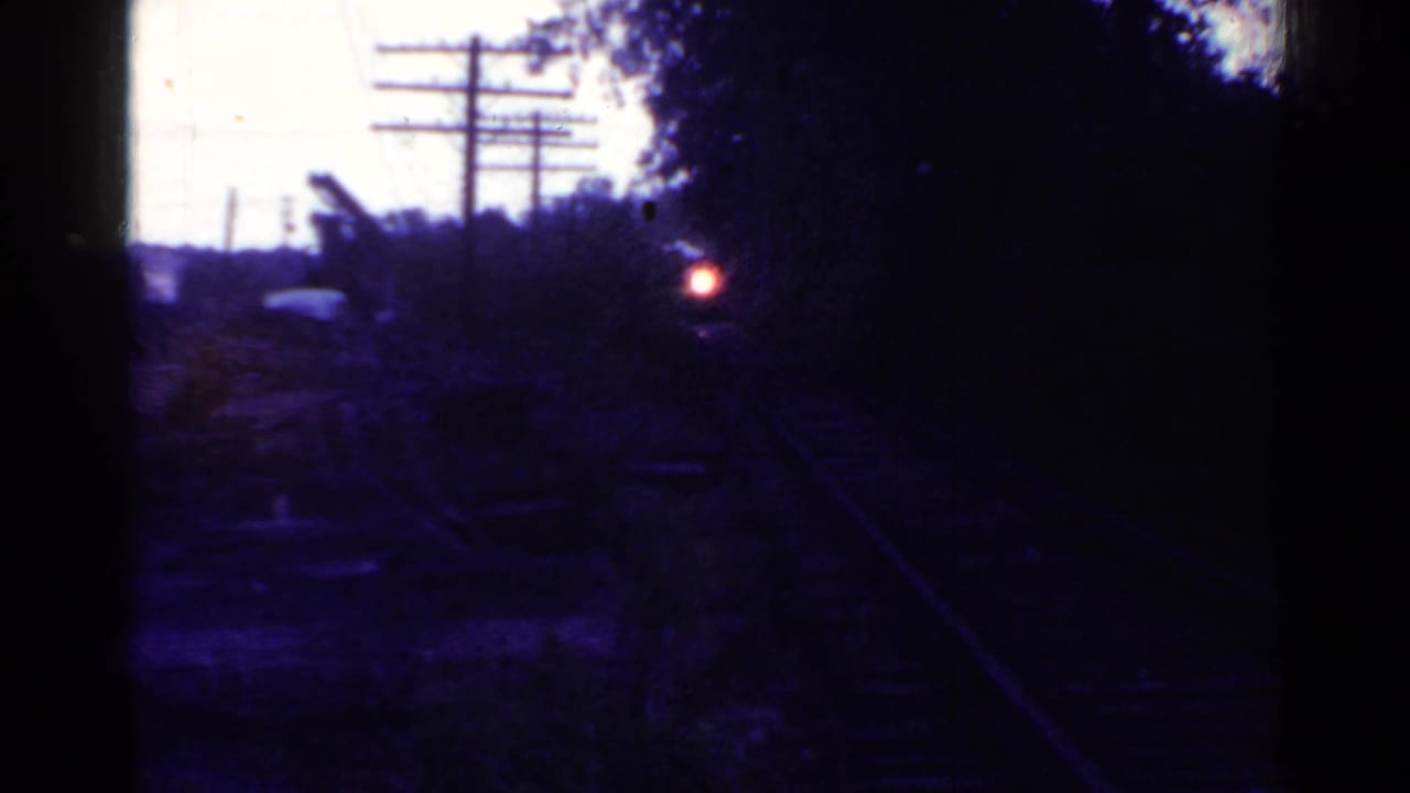 Dark 1953 Connecticut rail-yard view looking along tracks toward a small red rear light, with trees and utility poles silhouetted.
