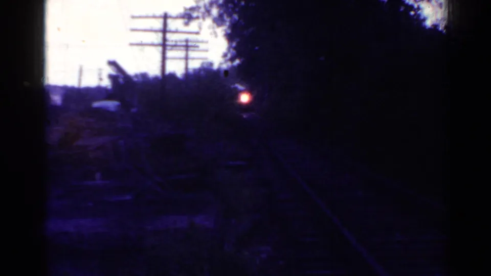 Dark 1953 Connecticut rail-yard view looking along tracks toward a small red rear light, with trees and utility poles silhouetted.