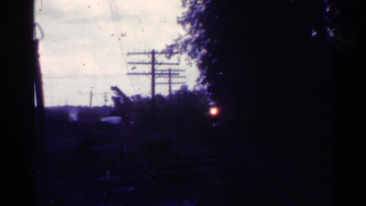 1953 Connecticut home-movie frame of a shadowed train-side view, with a red light near trees and telephone wires crossing the sky.