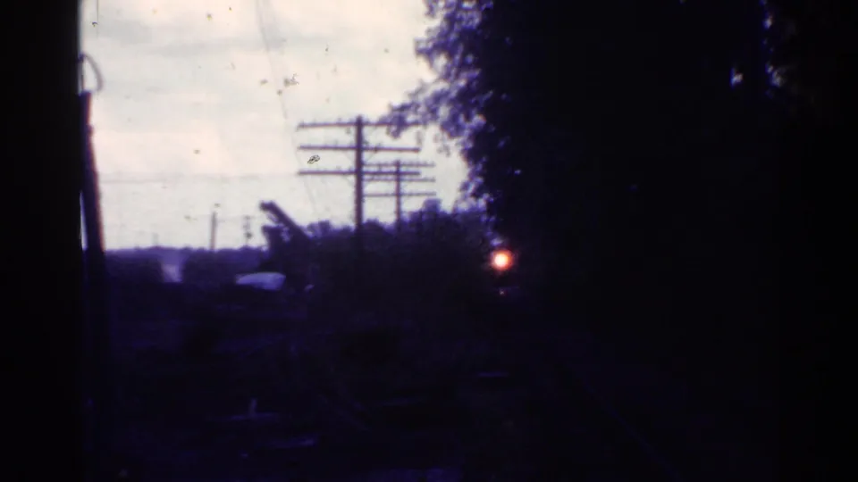 1953 Connecticut home-movie frame of a shadowed train-side view, with a red light near trees and telephone wires crossing the sky.