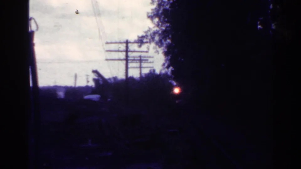 1953 Connecticut 8mm still with a stopped train area in shadow, telephone poles and wires beyond it, and a red light near the trees.