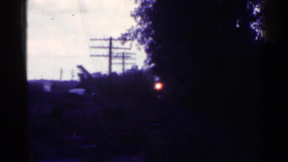 1953 Connecticut home-movie frame showing a dark, static rail-side scene with telephone wires, trees, and a glowing red light.
