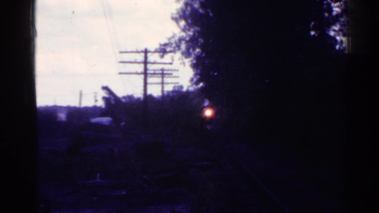1953 Connecticut 8mm frame showing dark railroad tracks, utility poles, trees, and an approaching train headlight at dusk.
