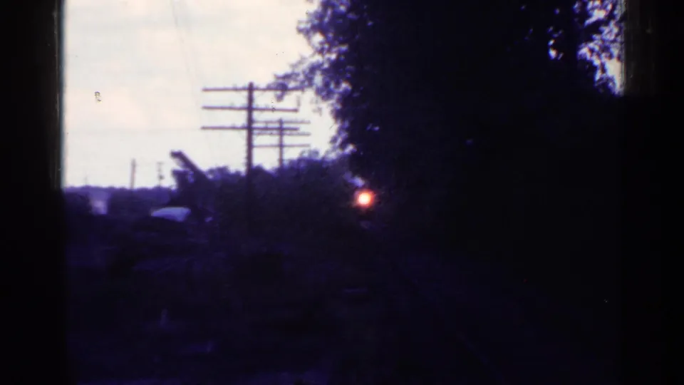 Connecticut 8mm footage frame with a train headlight glowing between trees and utility poles beside railroad tracks.