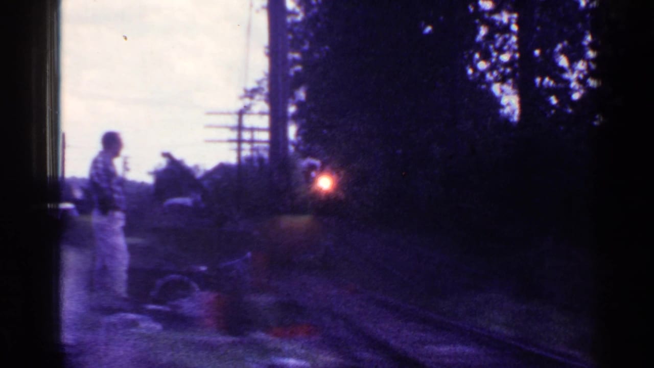 In Connecticut 1953 home-movie footage, a man in light pants stands near tracks while a steam locomotive approaches in dim light.
