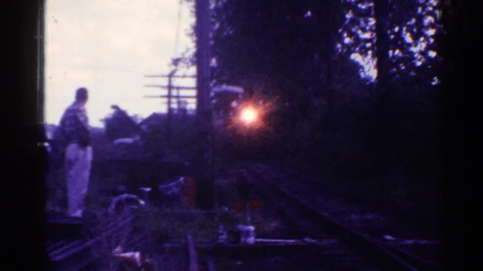 The man remains near the rails in Connecticut as the train headlight grows brighter against trees and brush.