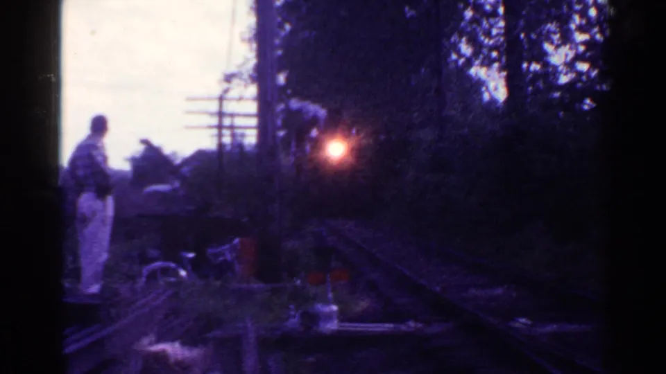 The 1953 Connecticut rail scene shows the man beside the line as the locomotive nears, framed by trees and dark 8mm shadows.