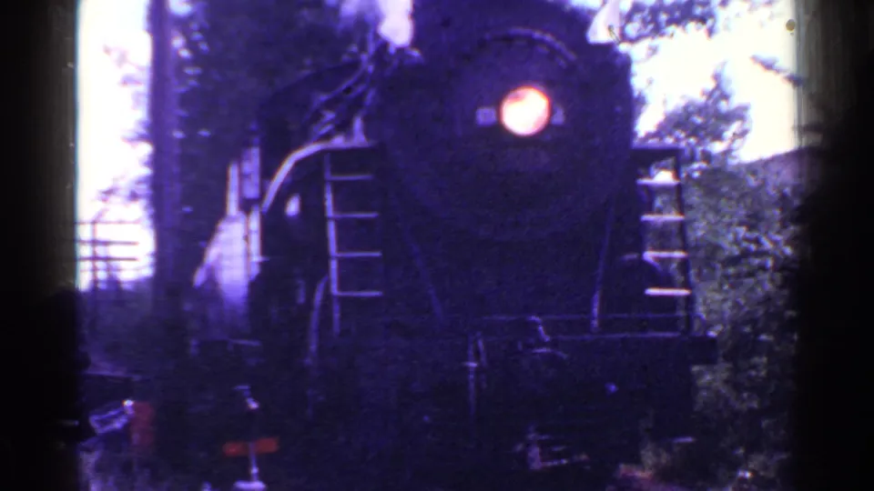 The locomotive advances closer in the 1953 Connecticut home movie, with its headlight, front handrails, smoke, and surrounding trees visible.